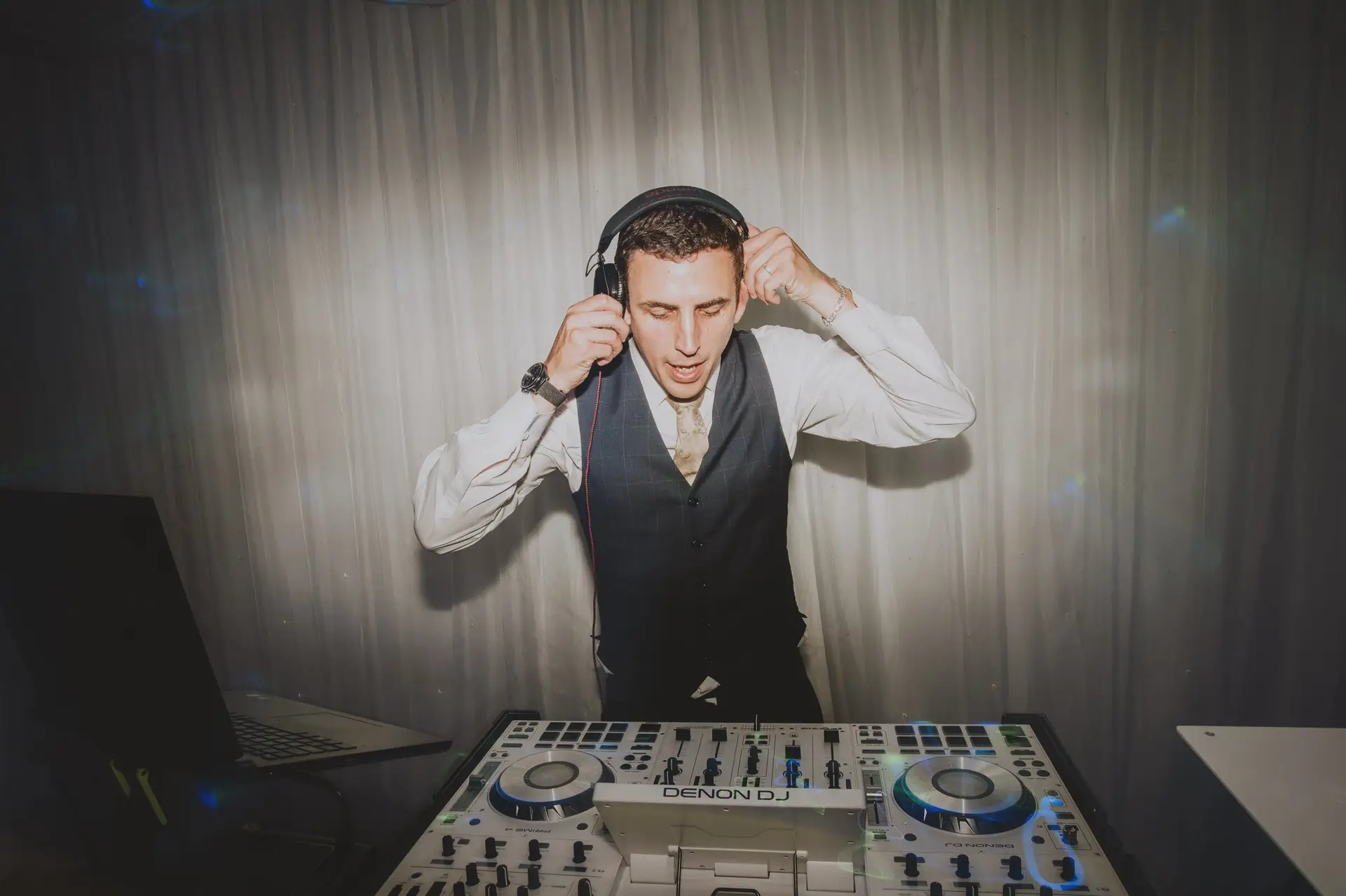 Dan at the decks in his waistcoat, headphones on