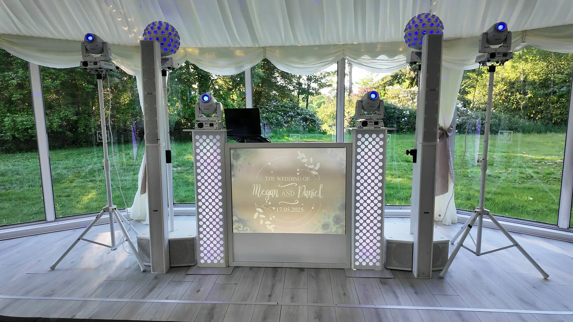 The all-white DJ setup in a glass-walled marquee, with trees and lawn outside