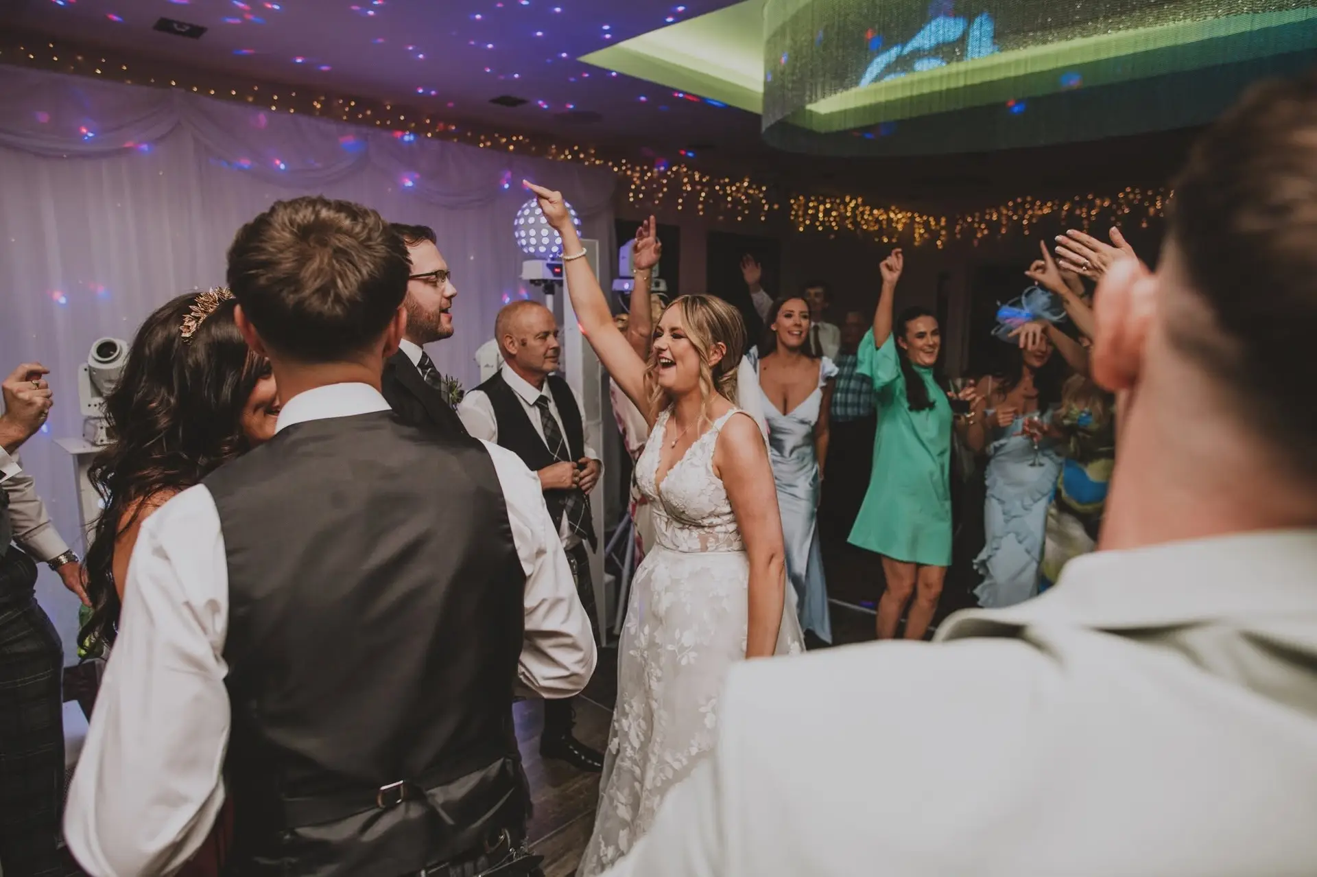 A laughing bride with her arm in the air among her guests on the dancefloor