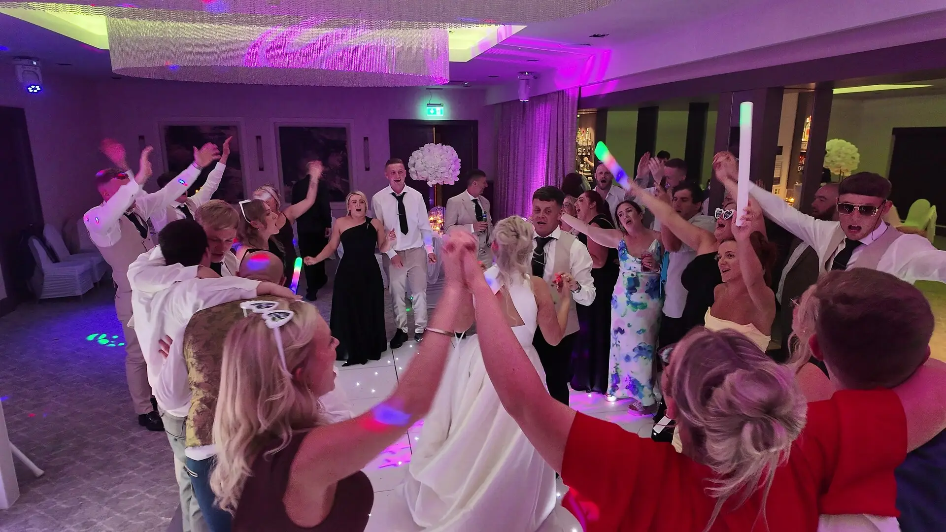 Wedding guests with their arms in the air around the bride on a packed dancefloor